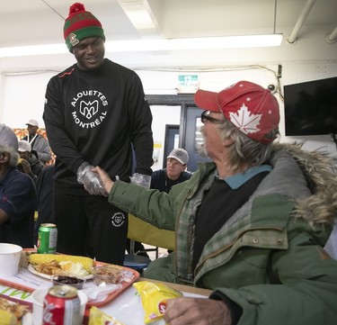 The Montreal Alouettes' T.D. Moultry stands up while shaking hands with a man as the player serves Thanksgiving dinner at the Welcome Hall Mission.