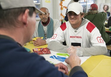 The Montreal Alouettes' Cody Fajardo, wearing a team outfit and a white cap, talks with a man as the player serves Thanksgiving dinner at the Welcome Hall Mission.