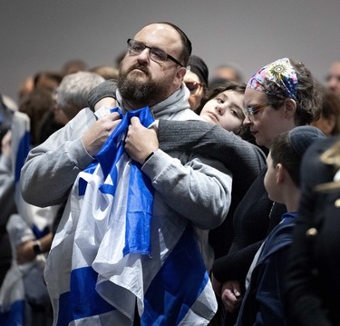A man clutches an Israeli flag as a child hugs him in a crowd at a vigil marking the deaths of over 800 Israelis in a Hamas attack.