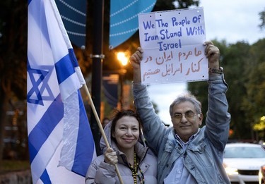 A man holds a multilingual sign reading "We the people of Iran stand with Israel" as a woman holds an Israeli flag outside a vigil marking the deaths of over 800 Israelis in a Hamas attack.