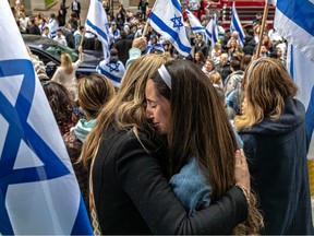 Two women embrace emotionally in a large crowd filled with Israeli flags at a rally in support of Israel..