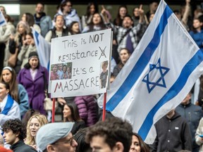 A sign reading "This is not resistance, it's a massacre" and an Israeli flag are seen in a large crowd of people at a demonstration in support of Israel.