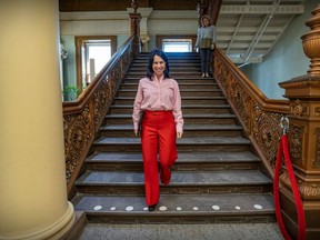 Valérie Plante descends a staircase wearing red pants and a pink shirt, smiling.