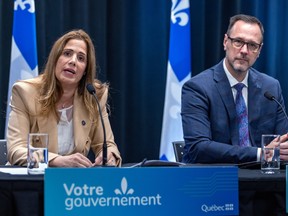 Pascale Déry and Jean-François Roberge sit at a table with Quebec flags behind them