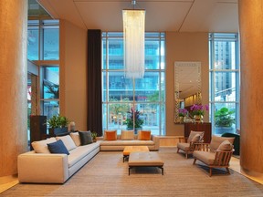 A lobby with a vertical chandelier and grey couches in front of large windows.