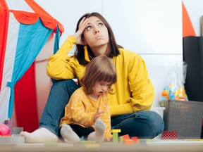 A woman in a yellow shirt rolls her eyes as the toddler in front of her plays with blocks.
