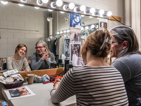 A woman and man smile while looking at themselves in a lit mirror backstage at the Segal Centre.