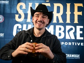 Arber Xhekaj, wearing a cowboy hat, smiles as he holds a burger