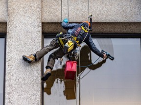 A window washer seen from behind, suspended on the side of a building.