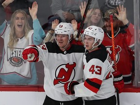 Devils' Tyler Toffoli and Luke Hughes embrace along the boards with cheering fans behind the glass
