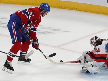 Montreal Canadiens' Sean Monahan and New Jersey Devils goaltender Vitek Vanecek reach for the puck with their sticks