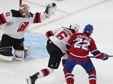 New Jersey Devils goaltender Vitek Vanecek extends his glove hand with the puck at the back of it as a Devils and Canadiens player fight for position