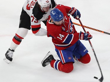 Canadiens' Nick Suzuki tries to control the puck while on his knees with Devils' Tyler Toffoli right behind him
