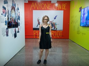 Maria Alyokhina stands in a room with exhibits on walls around her. Behind her reads the message "Anyone can be Pussy Riot".