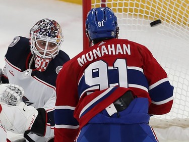 A puck in the air in the net is looked at by a Blue Jackets goaltender and Canadiens player