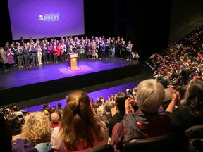 A large number of people gather on stage at a packed auditorium with the Bishop's University logo displayed on a large screen