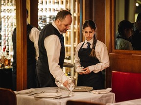 An older waiter shows a younger one how to set a table.