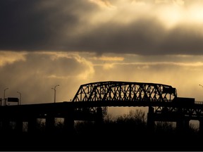 The superstructure of the Mercier Bridge is seen in silhouette under a cloudy yellowish-brown sky