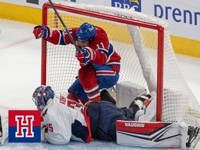 A hockey player celebrates a goal while standing inside the net above a fallen goalkeeper