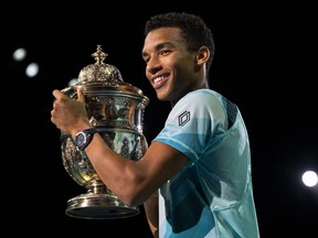 Felix Auger Aliassime smiles as he holds a large trophy