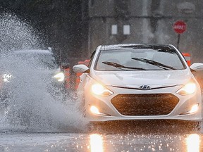 A white car drives through a puddle, splashing water higher than its roof.