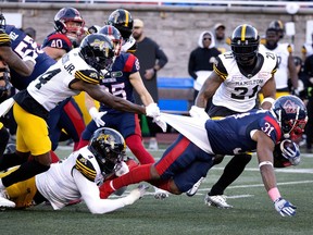 Hamilton Tiger-Cats' Dexter Lawson Jr. (14) and Jonathan Kongbo (4), bottom, grab hold of Alouettes running back William Stanback (31) during first half CFL football action in Montreal on Saturday, Oct. 28, 2023.