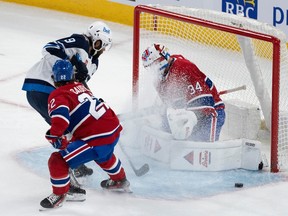 Canadiens goaltender Jake Allen (34) makes a save against Winnipeg Jets' Alex Iafallo (9) as Canadiens' Cole Caufield (22) skates in during first period NHL hockey action in Montreal on Saturday, Oct. 28, 2023.