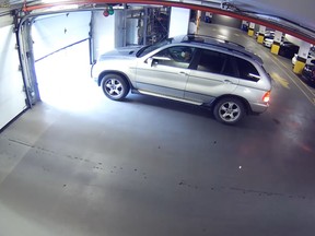 An SUV faces a garage door in an indoor parking garage, driven by a man in a face mask