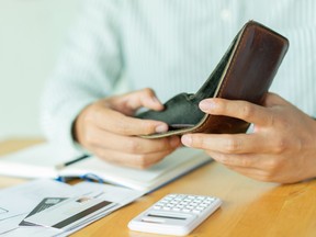 A man holds open an empty wallet on a table with a calculator and credit cards