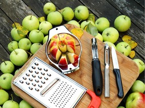 A cutting board rests on top of green apples. On the cutting board are tools to cut and grate apples.