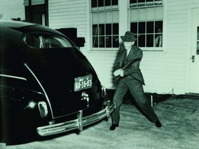 Henri Ford swings an axe at the back of a black car.