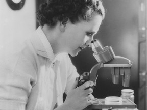 A black and white photo of a woman in profile looking into a microscope.