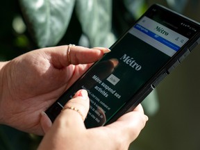 A person holds a phone displaying the home page of Métro Média, which reads in French that the company is suspending activities