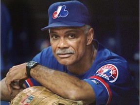 Expos manager Felipe ALou, wearing a baseball glove on his right hand, leans against a surface of the dugout and looks directly into the camera.