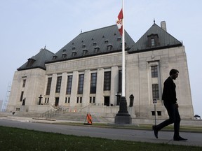 A man walks past the Supreme Court of Canada building, with a Canadian flag in the foreground.