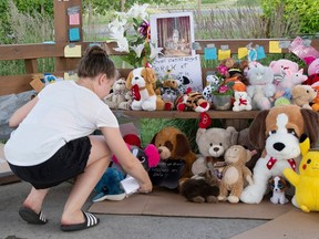 A teenager bends over to leave a message at a makeshift memorial composed of pictures and teddy bears