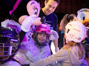 A girl in a skating helmet gets a hug from Minnie Mouse. There is another girl in a skating helmet reaching out to her.