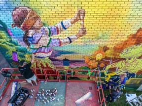 A man paints a mural of a child, blindfolded, playing a game.