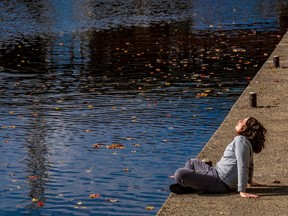 A woman tilts her face toward the sun as she sits cross-legged beside a pond.