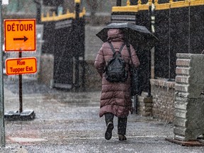 A woman walks on a sidewalk past a detour sign during a freezing rain storm