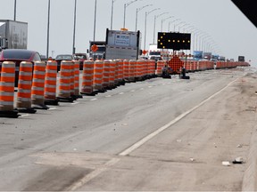 Construction cones line the side of a highway. There is an arrow directing traffic into other lanes.