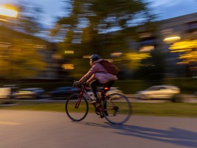 A cyclist in a pink coat rides past a blurred building.