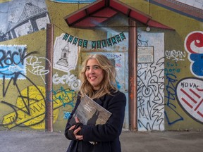A woman holds a book, with a mural behind her that says "Goose Village"