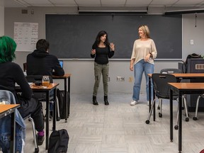 Two women stand at the front of a classroom while students sitting at desks watch