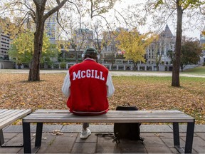 A student in a red McGill jacket, photographed from the back, sits on a bench on the grounds of McGill University on Nov. 3, 2023.