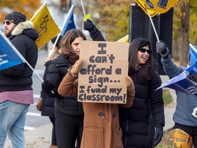 Striking teachers hold signs at a busy intersection in the Montreal borough of Lachine on Nov. 6, 2023.