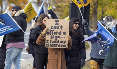 A teacher holds a sign that reads "I can't afford a sign ... I fund my classroom!" while striking