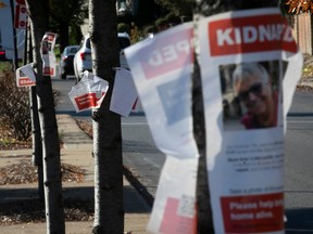 Posters of missing Israelis are attached to trees on a street. The word "Kidnapped" is at the top of the posters. Many of them are torn.