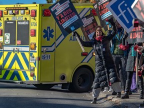 Striking health-care workers hold picket signs in front of an ambulance.
