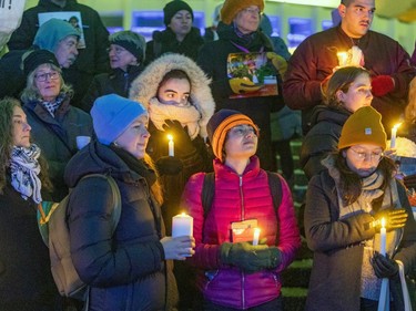 People bundled up for winter hold candles in front of them